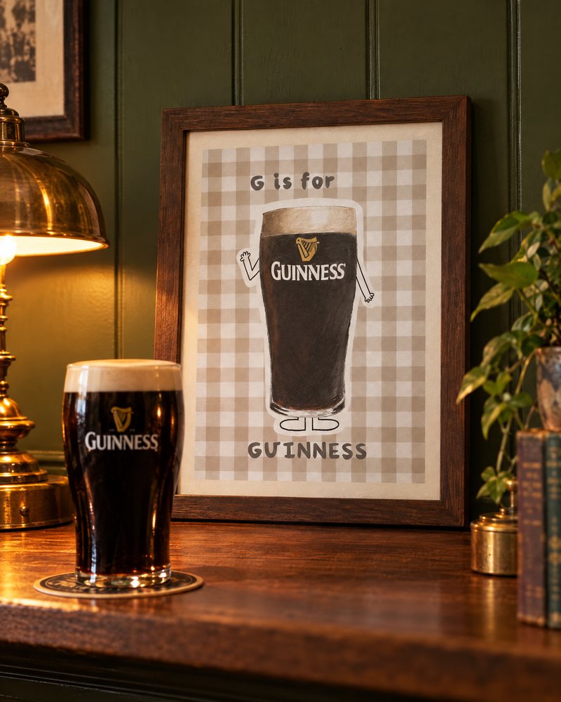 Framed G is for Guinness print on a wooden shelf beside a fresh pint